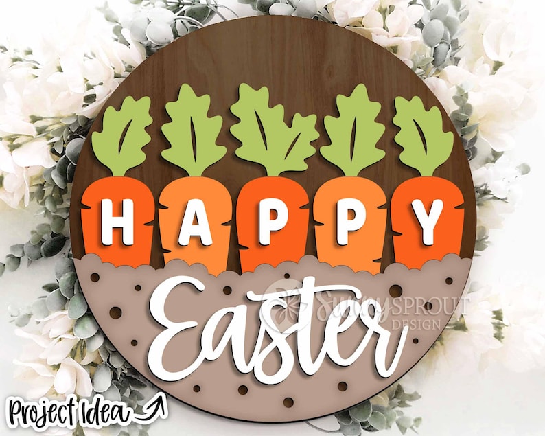 Pu&ograve; includere: Un cartello rotondo in legno con le parole "Happy Easter" in lettere bianche. Il cartello &egrave; decorato con cinque carote arancioni con cime verdi, disposte in fila.