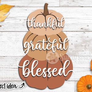 K&ouml;nnte beinhalten: Drei &uuml;bereinander gestapelte K&uuml;rbisse mit den Worten "thankful", "grateful" und "blessed" in wei&szlig; darauf. Die K&uuml;rbisse sind in Braun- und Oranget&ouml;nen bemalt.