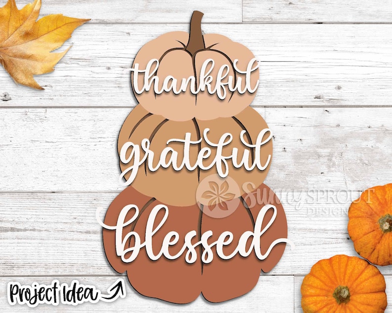 K&ouml;nnte beinhalten: Drei &uuml;bereinander gestapelte K&uuml;rbisse mit den Worten "thankful", "grateful" und "blessed" in wei&szlig; darauf. Die K&uuml;rbisse sind in Braun- und Oranget&ouml;nen bemalt.