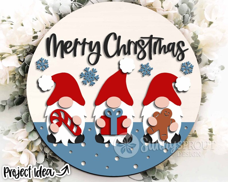 May include: A round wooden sign with the text "Merry Christmas" in black script. Three gnomes are depicted, each holding a different Christmas-themed item: a candy cane, a gift box, and a gingerbread man. The gnomes are red, white, and brown, and the background is blue with white snowflakes.