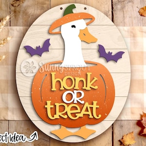 May include: A round wooden sign featuring a white goose wearing an orange hat, positioned inside a large orange pumpkin. The pumpkin displays the text "honk OR treat" in yellow and white lettering. Two purple bats flank the goose on the sign.