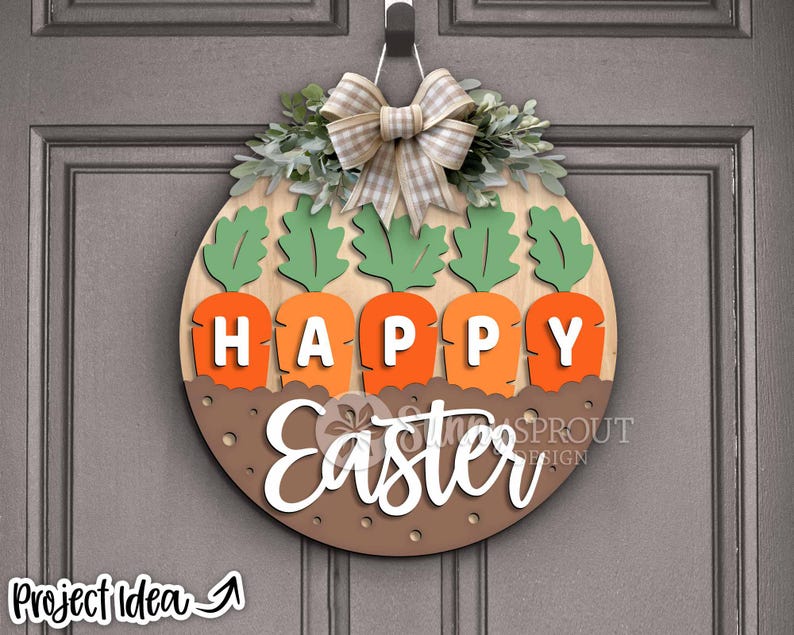 Pu&ograve; includere: Un appendiporta in legno con sfondo marrone e le parole "Happy Easter" in bianco. L'appendiporta &egrave; decorato con foglie verdi, un fiocco bianco e marrone e cinque carote arancioni con cime verdi.
