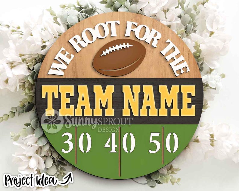 May include: A circular wooden sign featuring a brown football graphic and the white text "WE ROOT FOR THE" above the yellow text "TEAM NAME" on a dark background, with a green field graphic at the bottom displaying the white numbers 30, 40, and 50.