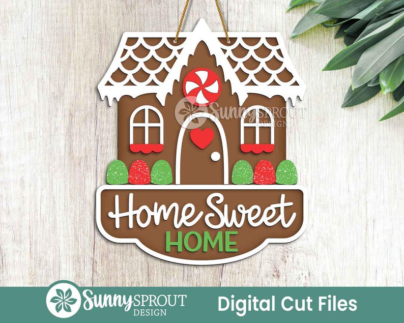 May include: A brown gingerbread house-shaped sign with white accents, a red heart, and a candy swirl. The sign reads "Home Sweet Home" in white script with green lettering. The sign is hanging by a gold string.