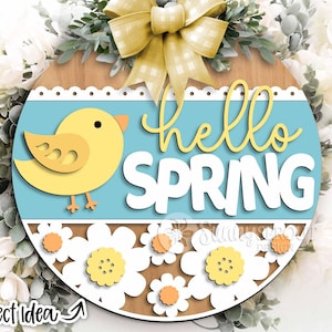 May include: A round wooden sign with a blue background and the text "hello spring" in white. The sign is decorated with a yellow bird, white flowers, and a yellow bow.