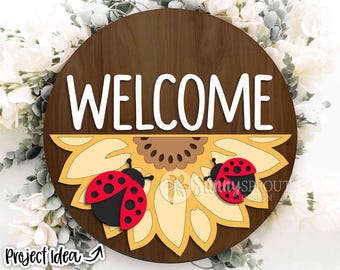 May include: A wooden round sign with the word "WELCOME" in white letters. The sign is decorated with a yellow sunflower with two red ladybugs on it.