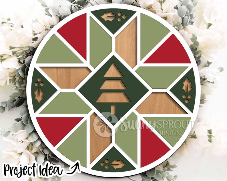 May include: Circular wooden Christmas ornament with a geometric design. The ornament features red, green, and natural wood tones, with a Christmas tree cutout in the center. The text "Project Idea" is visible on the bottom left.