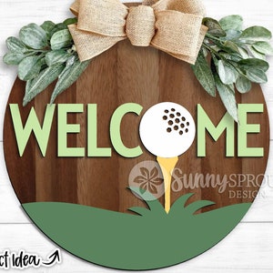May include: A round wooden door hanger with the word "WELCOME" in green letters. A golf ball with a yellow tee is in the center of the sign. The background is a wood grain pattern.