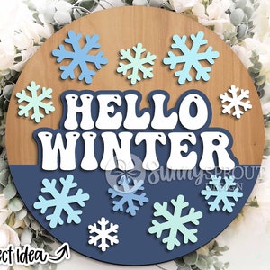 May include: A round wooden sign with a blue and white color scheme. The sign says "Hello Winter" in white letters with a blue background. The sign is decorated with snowflakes in various shades of blue and white.
