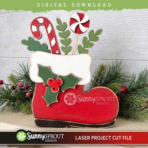 May include: A red wooden Christmas stocking cutout featuring a white cuff, green holly leaves with red berries, a candy cane, and a peppermint lollipop. The text SunnySprout DESIGN is printed on the front of the stocking, which is a digital download.