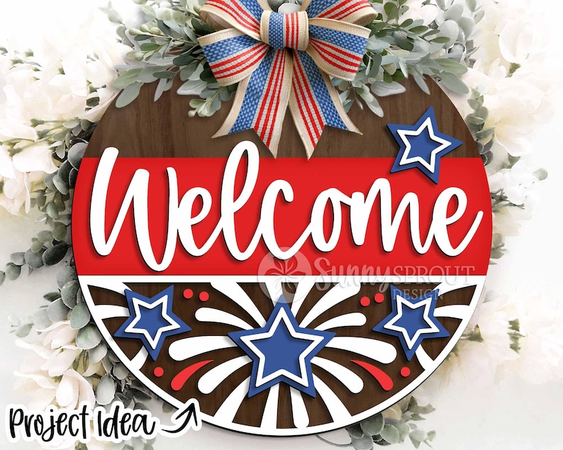 May include: A round wooden sign with a red, white, and blue patriotic theme. The sign says "Welcome" in white letters and features a firework design with stars.