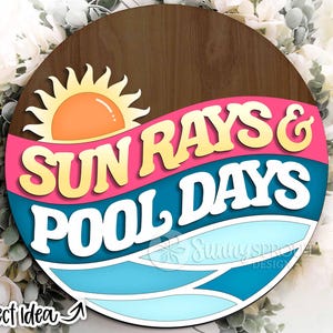 May include: A round wooden sign with the words "SUN RAYS & POOL DAYS" in a retro font. The sign features a sun graphic and a blue and pink wave design, evoking a summer theme. The sign is surrounded by white flowers.