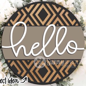 May include: A round wooden sign with a geometric pattern in black and brown. The word "hello" is written in white cursive on a brown background.