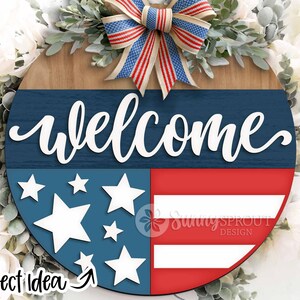 May include: A wooden welcome sign with a red, white, and blue American flag design. The sign features a blue background with white stars and a red and white striped section. The word "welcome" is written in white cursive letters on the blue background. The sign is decorated with a red, white, and blue bow.