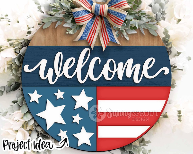 May include: A wooden welcome sign with a red, white, and blue American flag design. The sign features a blue background with white stars and a red and white striped section. The word "welcome" is written in white cursive letters on the blue background. The sign is decorated with a red, white, and blue bow.