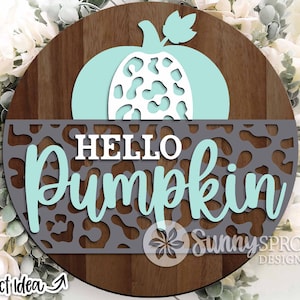 May include: A round wooden sign with a teal pumpkin design and the words "HELLO PUMPKIN". The sign has a gray leopard print pattern and is surrounded by greenery. The sign is a project idea from Sunny Sprout Design.