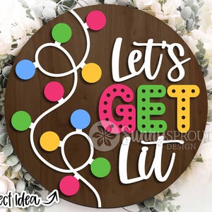 May include: A brown wooden round sign with the text "Let's Get Lit" in white, green, pink, and yellow letters. The letters are decorated with white polka dots. A white string of colorful lights is wrapped around the sign.