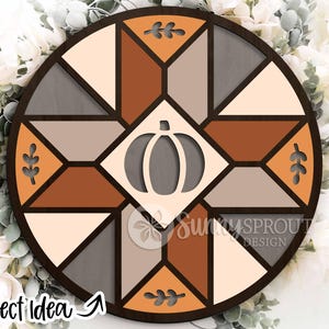 May include: A round wooden wall decor piece with a geometric design in shades of brown, gray, and cream. A pumpkin cutout is centered, and leaf cutouts are placed around the perimeter. The text "Project Idea" is visible.