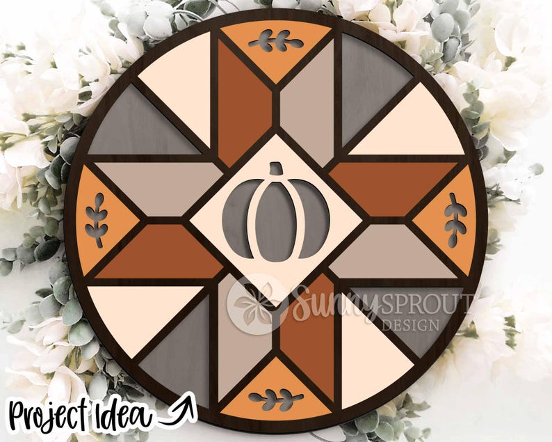 May include: A round wooden wall decor piece with a geometric design in shades of brown, gray, and cream. A pumpkin cutout is centered, and leaf cutouts are placed around the perimeter. The text "Project Idea" is visible.