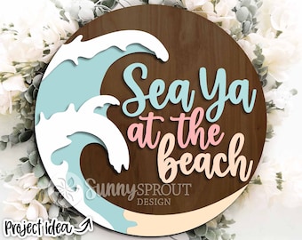 May include: A round wooden sign with a blue and white wave design and the text "Sea Ya at the Beach".