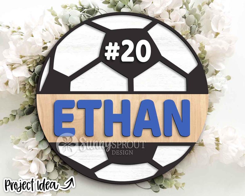 May include: A wooden soccer ball design with the name "ETHAN" in blue letters and the number "20" in white. The design is set against a light wood background and a black soccer ball pattern. The words "Sunny Sprout Design" are also visible.