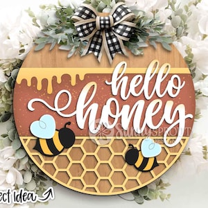 May include: A round wooden sign with the words "hello honey" in white script. The sign features a honeycomb pattern, two cartoon bees, and a dripping honey design. A black and white checkered bow and greenery are at the top.