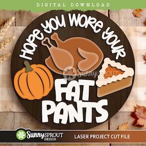 May include: A circular wooden sign featuring the white text Hope you wore your fat pants, a brown roasted turkey, an orange pumpkin, and a slice of pumpkin pie. The design is a digital download for laser cutting projects with a dark wood grain background.