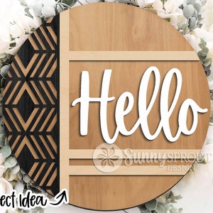 May include: A round wooden sign with a geometric pattern on the left side and the word "Hello" in white cursive lettering on the right side. The sign has a light brown wood grain and a dark brown border.