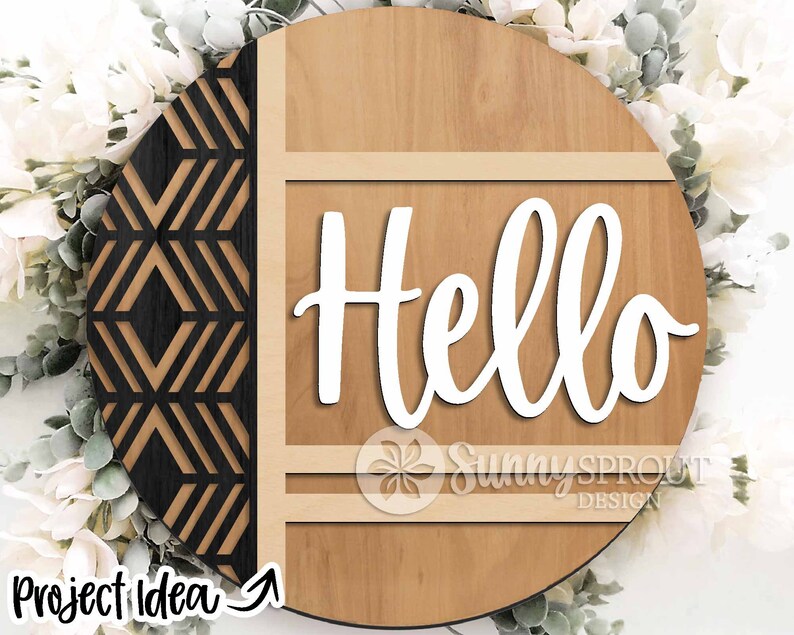 May include: A round wooden sign with a geometric pattern on the left side and the word "Hello" in white cursive lettering on the right side. The sign has a light brown wood grain and a dark brown border.