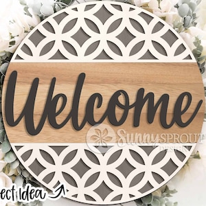 May include: A round wooden sign with a gray and white geometric pattern. The sign says "Welcome" in black cursive lettering.