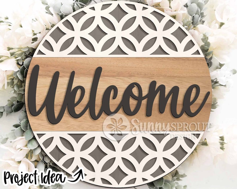 May include: A round wooden sign with a gray and white geometric pattern. The sign says "Welcome" in black cursive lettering.