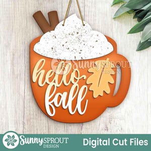 Op de afbeelding: Houten bord in de vorm van een koffiekopje met de tekst "hello fall". Het kopje is oranje met een witte slagroomtopping en kaneelstokjes. Een blad is ook in het ontwerp opgenomen. Het bord hangt aan een touwtje. Herfstthema.