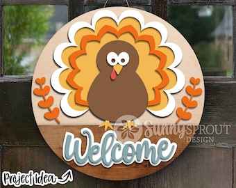 Puede incluir: Un colgador de puerta redondo de madera con un pavo marrón con plumas naranja y amarillas. El pavo tiene grandes ojos blancos y una papada roja. Las palabras "Bienvenido" están escritas en azul en la parte inferior del colgador de puerta.
