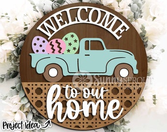 May include: A round wooden sign with a light blue pickup truck carrying colorful Easter eggs. The sign says "Welcome to our home" with a woven pattern underneath the text.