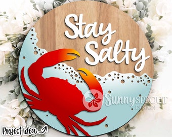 May include: A round wooden sign with the text "Stay Salty" in white lettering. A red crab with orange accents is in the lower left corner of the sign, surrounded by blue and white waves.