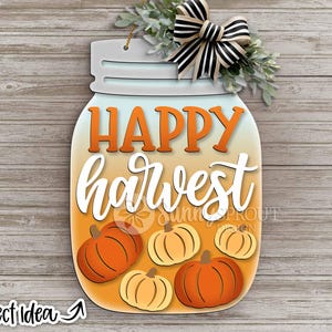 Op de afbeelding: Een houten bord in de vorm van een weckpot met de woorden "HAPPY HARVEST" in oranje en wit. Het bord heeft oranje en gele pompoenen, een zwart-wit gestreepte strik en groen. De woorden "Project Idea" staan in de linker benedenhoek.