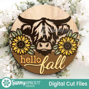 Puede incluir: Un letrero redondo de madera con la silueta de una vaca de las Tierras Altas y girasoles. Las palabras "hello fall" están escritas en una fuente cursiva. El letrero está rodeado de flores blancas y vegetación. También se ve el texto "Sunny Sprout Design" y "Digital Cut Files".