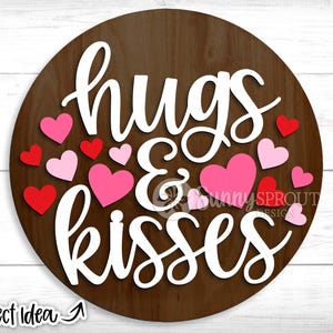 May include: A brown wooden round sign with the words "hugs & kisses" in white lettering. The sign is decorated with pink and red hearts.