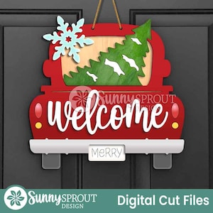 May include: A red wooden truck-shaped door hanger with a Christmas tree and snowflake design. The word "welcome" is written in white script across the truck. A small sign reads "MERRY". The door hanger is suspended by a gold string.