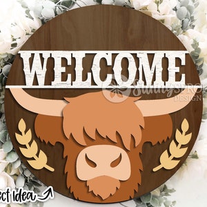 Peut inclure: Une pancarte ronde en bois avec un fond brun et une inscription blanche "WELCOME". La pancarte repr&eacute;sente une t&ecirc;te de vache Highland brune et orange avec des &eacute;pis de bl&eacute; de chaque c&ocirc;t&eacute;.