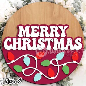May include: A round wooden sign with a red background and white text that reads "Merry Christmas". The sign is decorated with a string of colourful lights.