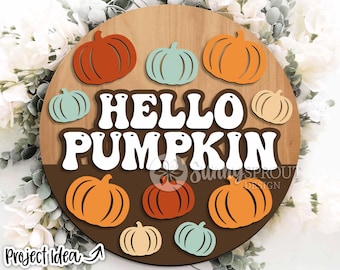 May include: A wooden round sign with the text "HELLO PUMPKIN" in white letters. The sign is decorated with orange and green pumpkins.