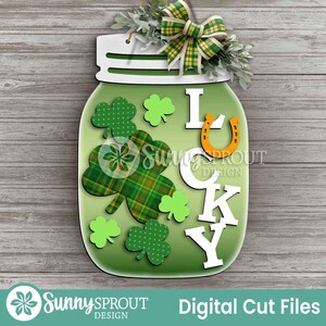 May include: A green mason jar-shaped St. Patrick's Day decoration with the word "LUCKY" in white letters. The jar features shamrocks, a horseshoe, and a plaid shamrock. A green and yellow plaid bow and greenery adorn the top.