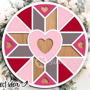 May include: A round, multi-colored wooden wall art piece with a heart design. The art features a central heart shape, surrounded by geometric shapes in shades of red, pink, gray, and wood tones. The text "Project Idea" is visible at the bottom left.