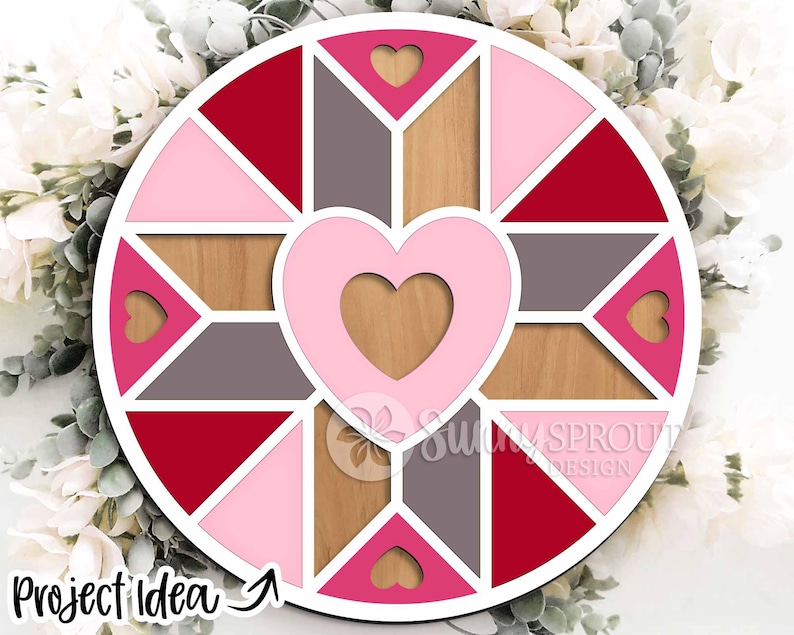May include: A round, multi-colored wooden wall art piece with a heart design. The art features a central heart shape, surrounded by geometric shapes in shades of red, pink, gray, and wood tones. The text "Project Idea" is visible at the bottom left.