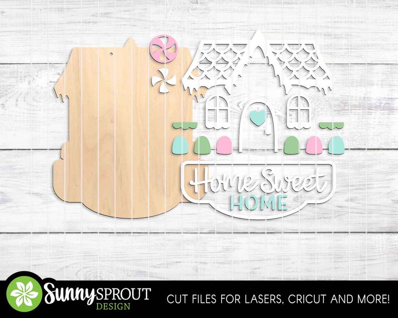 May include: Wooden house-shaped cutout with a decorative white house overlay. The overlay features windows, a heart, and the words "Home Sweet Home." Accents include pink, green, and blue elements. The design is for laser cutting and crafting.