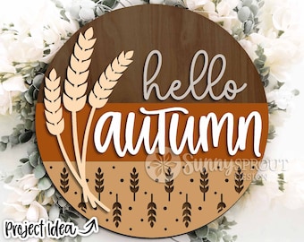 May include: A round wooden sign with the text "hello autumn" in white lettering. The sign is decorated with a brown and orange background and a pattern of wheat stalks.