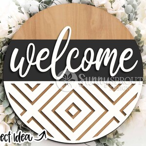 May include: A round wooden sign with a black and white geometric pattern. The top half of the sign is wood with a black band and the word "welcome" in white cursive lettering. The bottom half of the sign is a white geometric pattern with black lines.