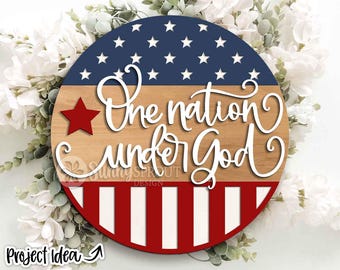 May include: A round wooden sign with a patriotic design. The top section is navy blue with white stars, the middle is light brown, and the bottom has red and white stripes. The words "One nation under God" are written in white script.