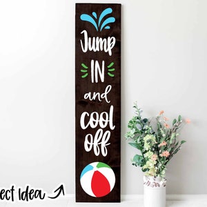 May include: A wooden sign with the text "Jump In and Cool Off" in white lettering. The sign features a blue water splash design at the top and a red, white and blue beach ball at the bottom.